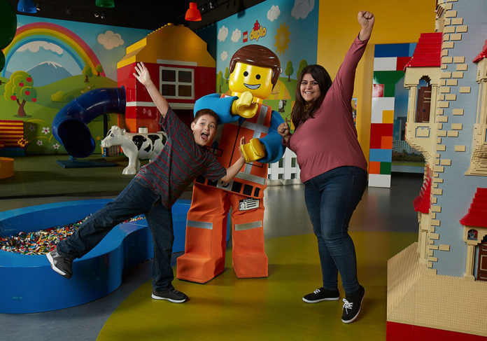 A family enjoying Legoland Discovery Center in Schaumburg, Illinois, posing with a life-sized Lego character in a colorful indoor play space filled with interactive Lego exhibits and creative play areas.