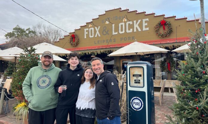 A family posing in front of Fox & Locke in Leiper’s Fork, Franklin, Tennessee, a kid-friendly restaurant and live music venue decorated for the holidays.